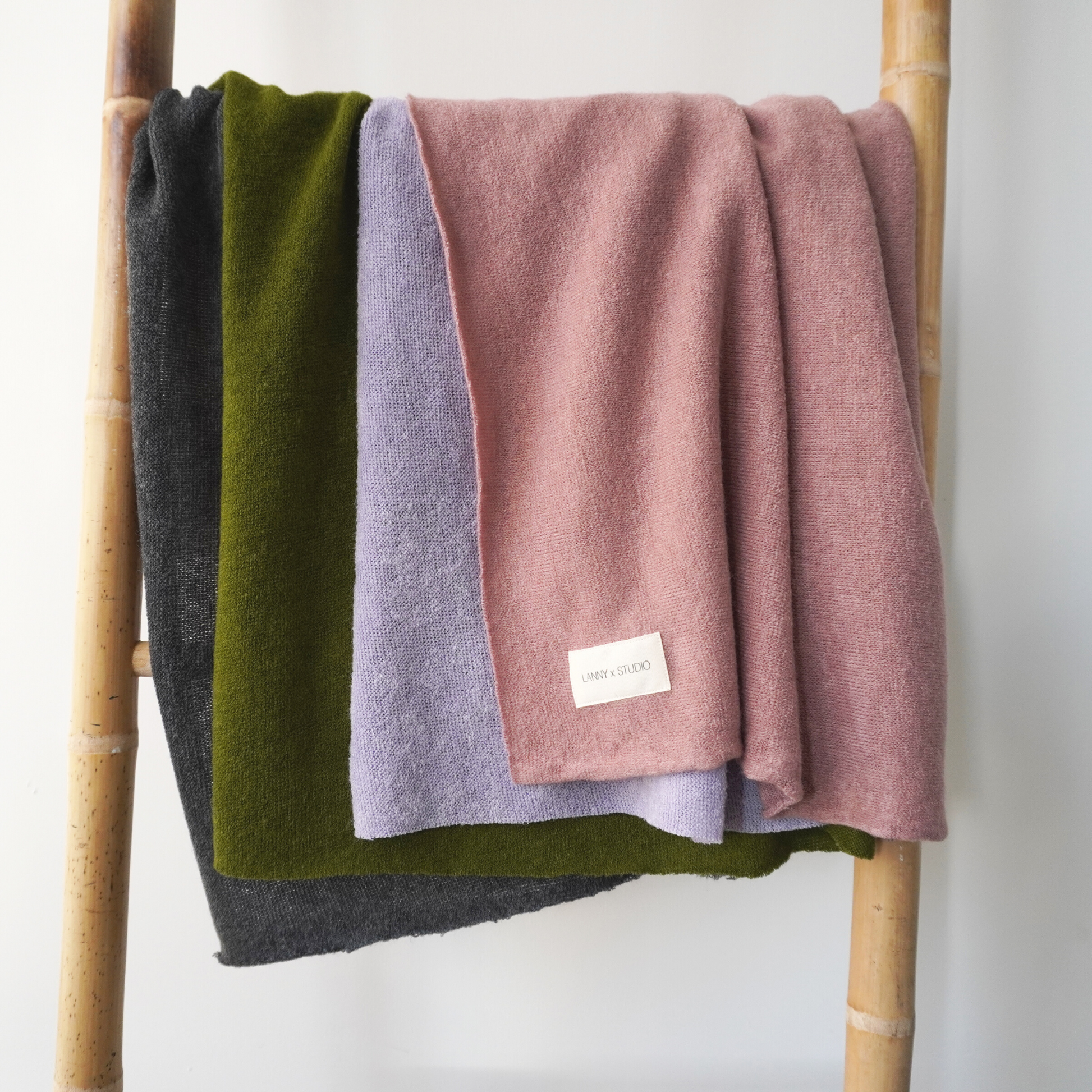 Pink, Green, Lilac and charcoal colour block throw in knit fabric. Hanging on wooden ladder. 