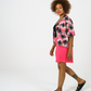 Bright pink Tye dye printed women shirt with black palms paired with our bright pink jersey shorts. Styles over a black bodysuit and sandals.