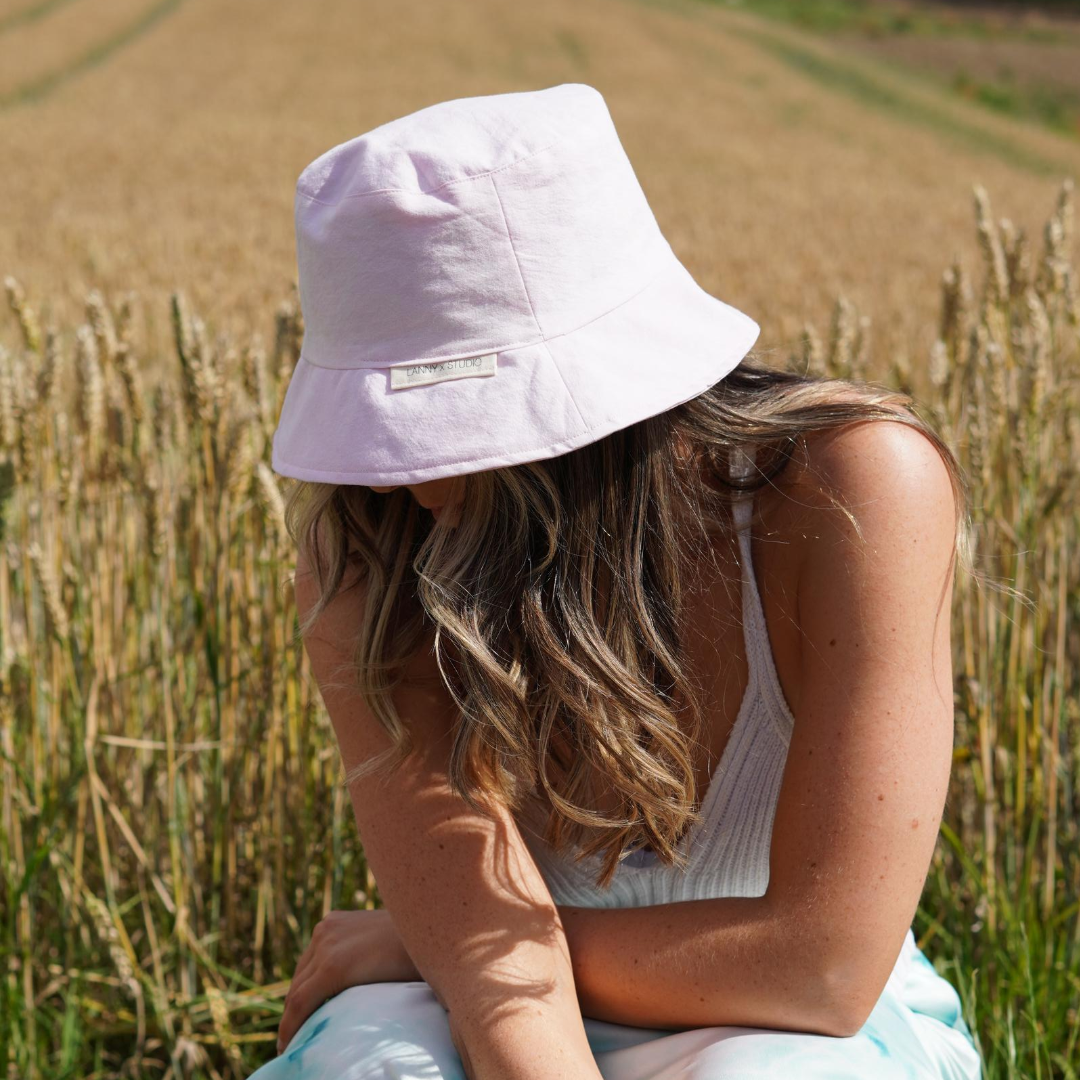 Light pink bucket hat with a subtle acid wash finish, photographed on a female with a wheat field in the background. 