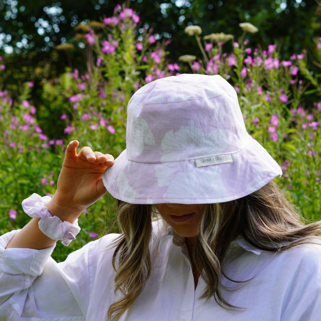 Lilac and White Floral Bucket Hat, photographed on a women wearing a matching scrunchie on wrist. 