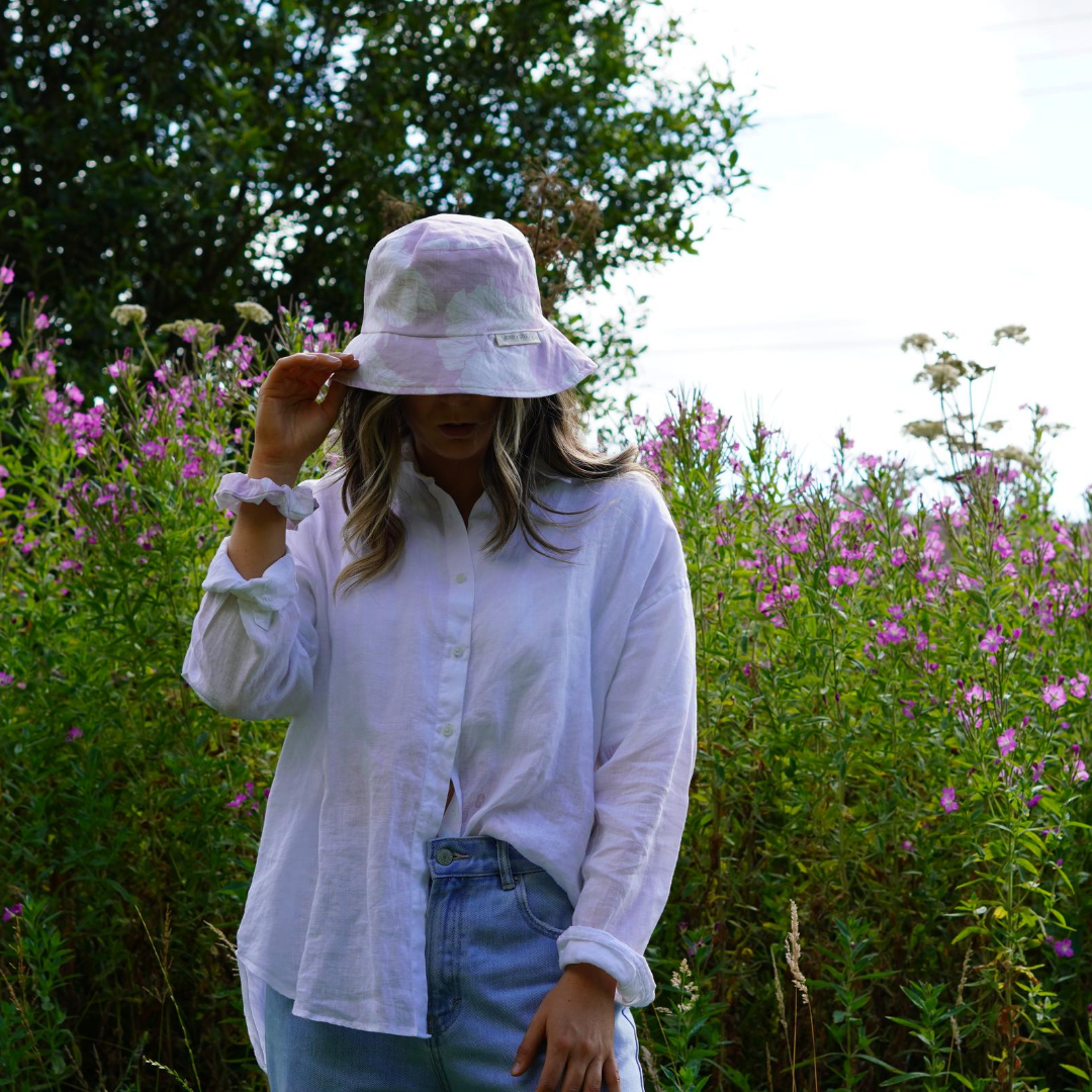 Lilac and White Floral Bucket Hat, photographed on a women wearing a white shirt and matching scrunchie on wrist. 