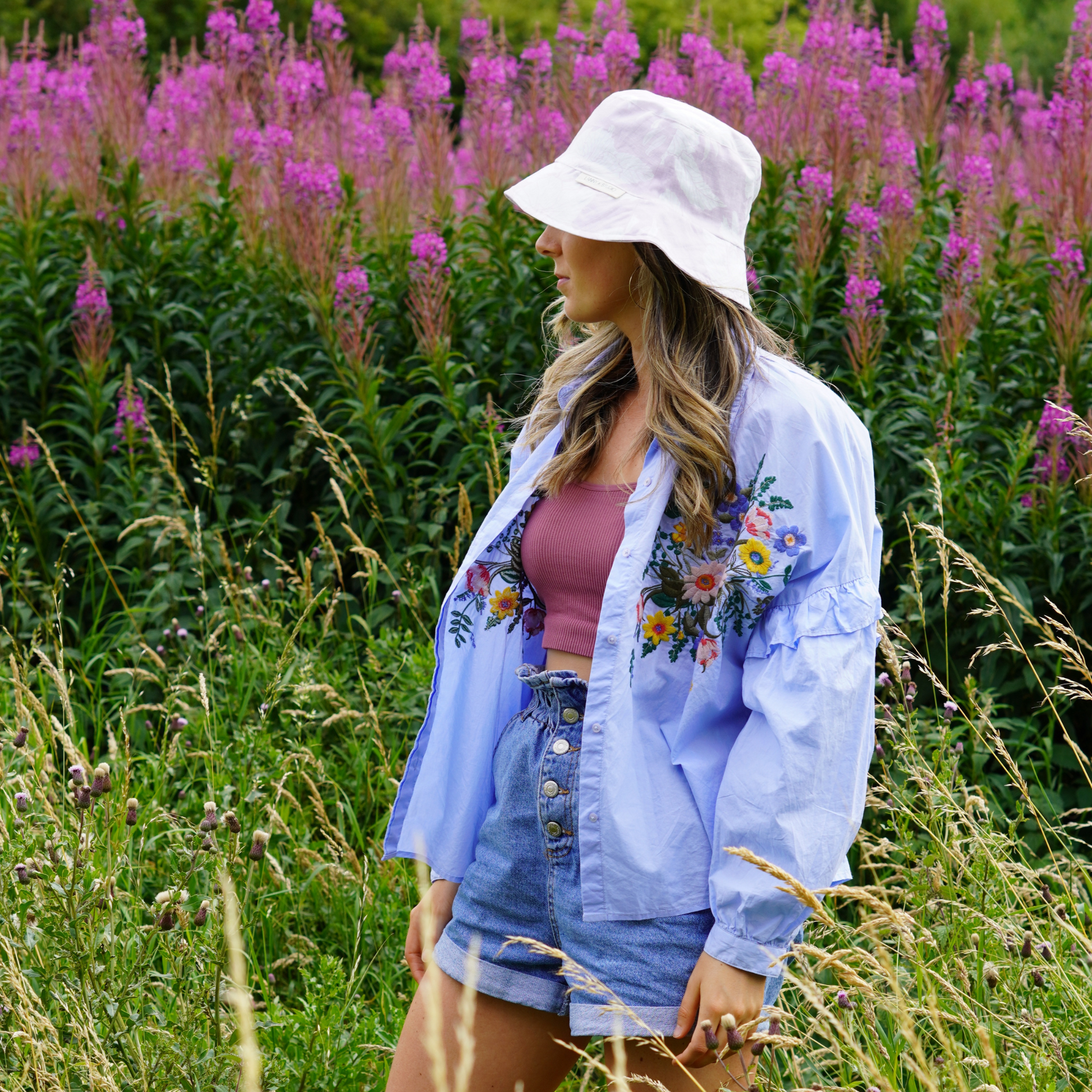 Lilac and White Floral Bucket Hat, photographed on a women looking at the flowers behind her. 