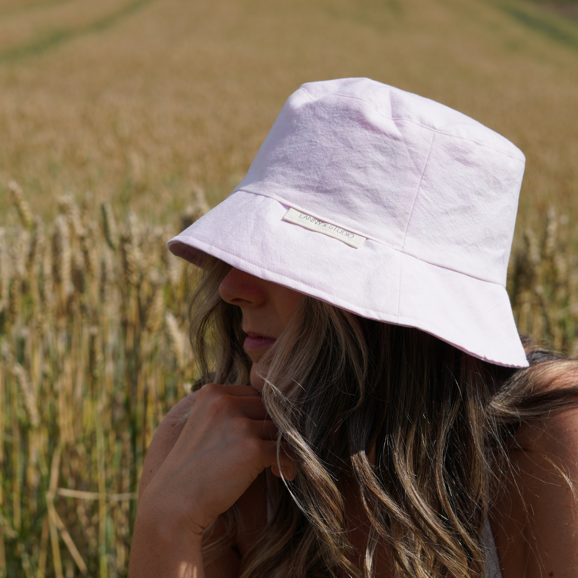 Light pink bucket hat with a subtle acid wash finish, photographed on a female with a wheat field in the background. 