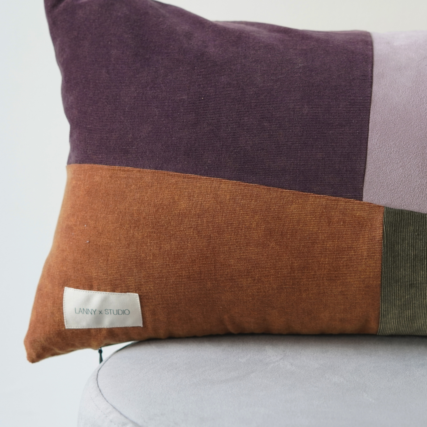 Orange, Purple, Green and Lilac panelled rentable cushion with branded LannyxStudio label. Close up view of orange and purple panels. 