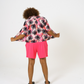 Back view of our bright pink Tye dye printed women shirt with black palms paired with our bright pink jersey shorts paired with black sandals. 