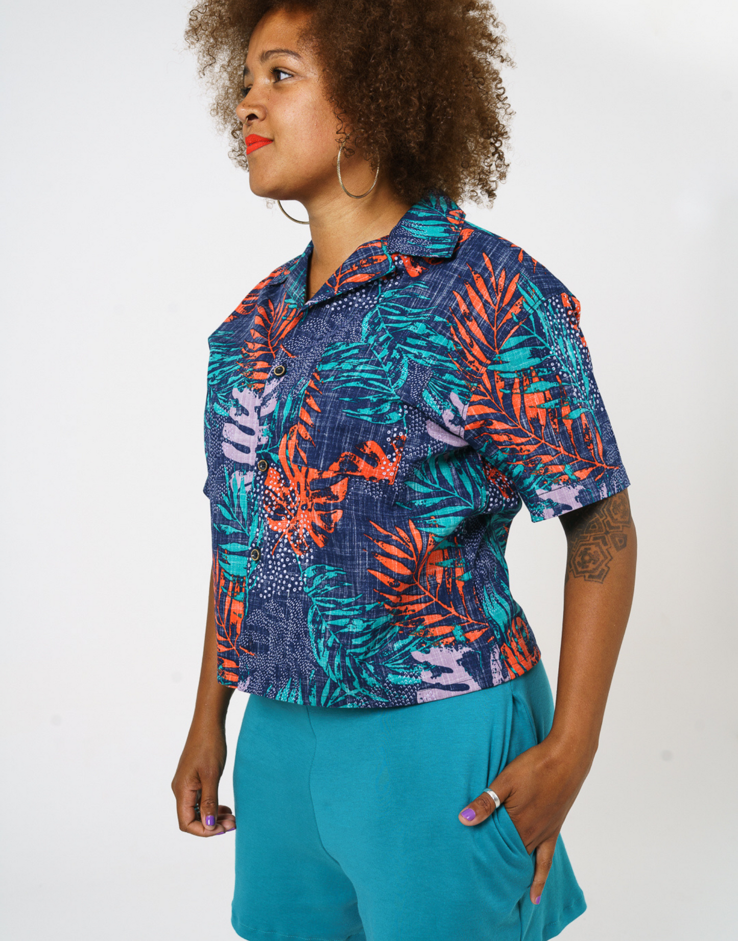 Close up of our digitally printed cotton womens shirt in bright teal and orange leaf print and revere collar details. Paired with our teal Jersey shorts and styles with Bright trainers and socks. 
