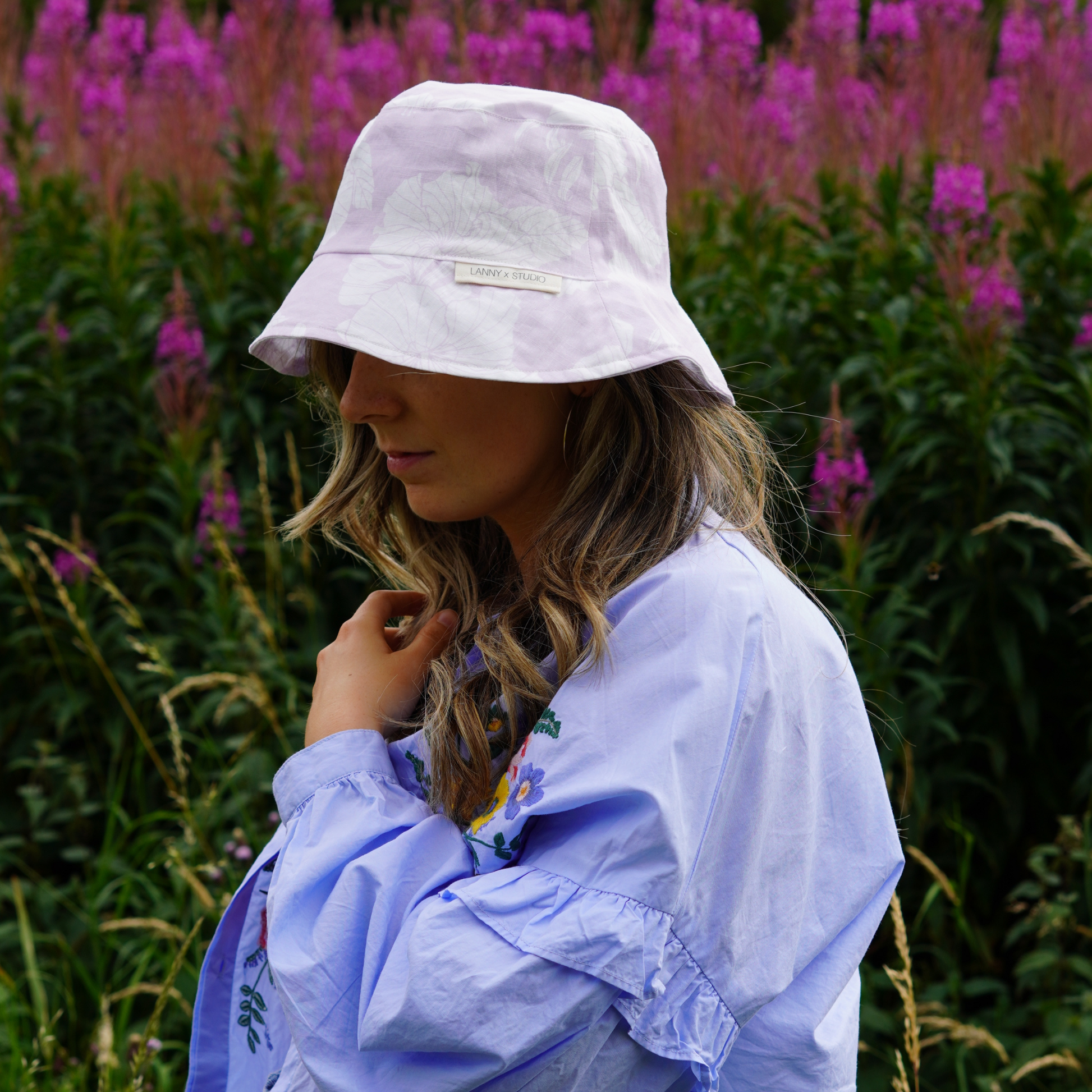 Lilac and White Floral Bucket Hat, photographed on a female with a flowery background. 