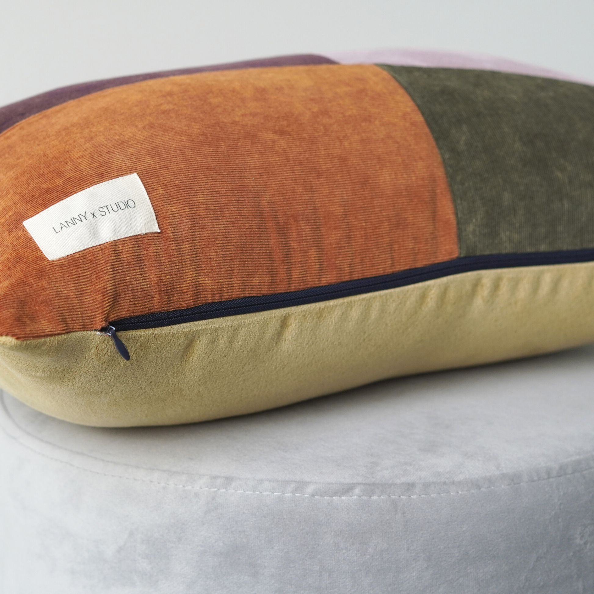 Orange, Purple, Green and Lilac panelled rentable cushion with branded LannyxStudio label. Backed in yellow suede look fabric and contrast navy zip. Close up view of zip feature. 