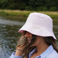 Light pink bucket hat with a subtle acid wash finish, photographed on a female looking to the side with hair blowing in the wind. 