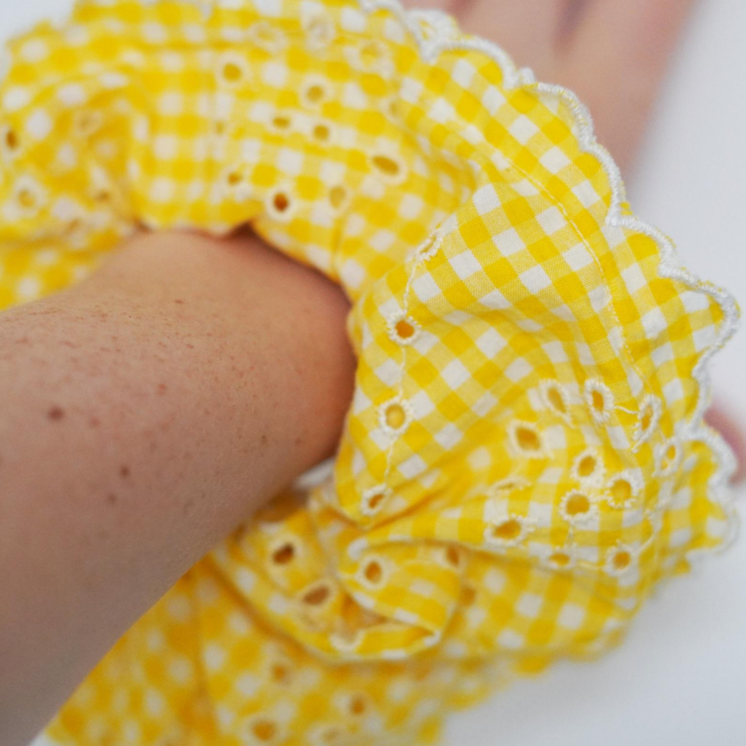 Close up view of yellow and white gingham and broiderie anglaise extra large scrunchie with scalloped edge on wrist.  